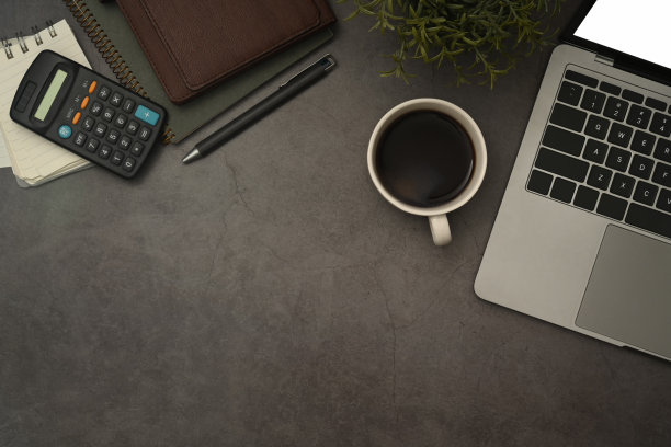 笔记本电脑，咖啡杯，计算器和笔记本电脑上的黑色石板石背景。平铺，俯视图。图片下载