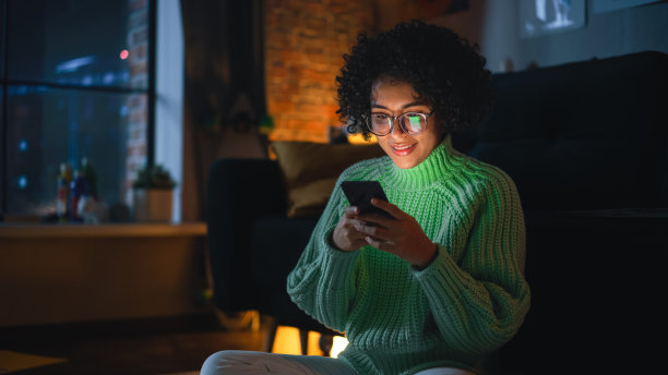 晚上在家里用智能手机打字的拉丁专注女人。网络成瘾女性使用手机应用程序进行网上购物，社交媒体，浏览。图片下载