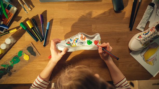 俯视图女设计师创造手工制作的鞋子，在家里画画。女人在桌子上工作。鞋类定制和创意职业概念。关闭了。图片下载