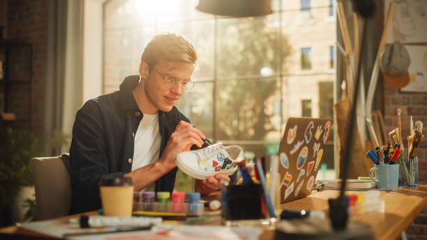 男时装设计师在他的工作场所为旧运动鞋创造新的设计。少年艺术家专注于他的工作。定制和环保时尚服装概念。图片下载