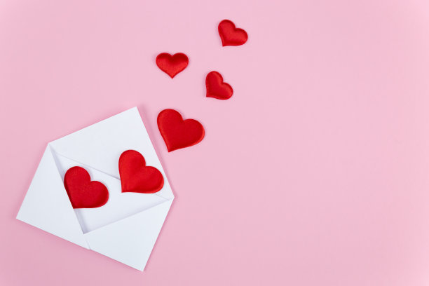 红心从粉色背景的白色信封里掉出来。情人节图片下载
