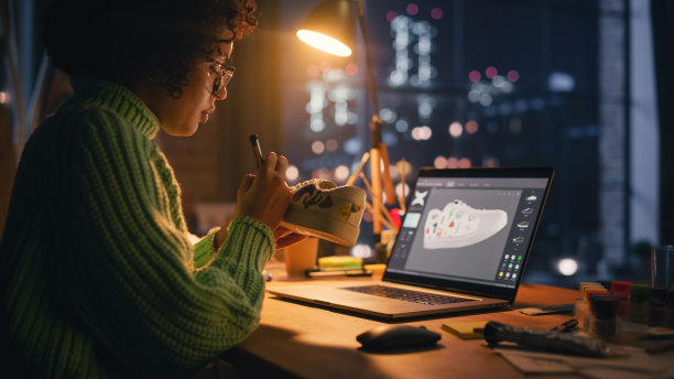 侧视图活跃的女设计师坐在阁楼工作室晚上和工作在她的笔记本电脑前的鞋子定制。新一代潮流时装设计理念。图片下载