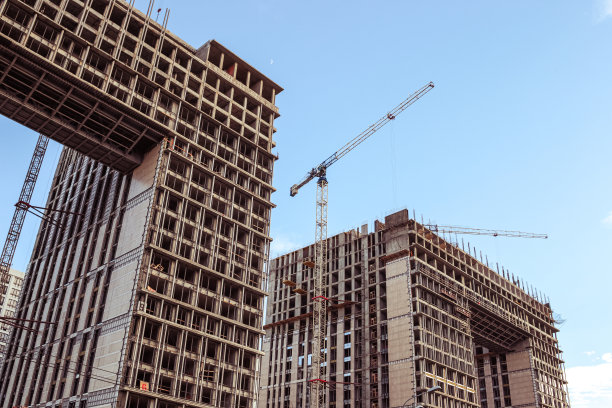 建筑工地。蓝天背景下的建筑起重机和正在施工的建筑。建筑起重机正在工作，建筑物的墙壁正在竖起。图片下载