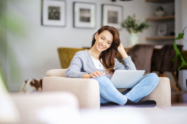 微笑的白人妇女使用笔记本电脑在家里坐在扶手椅上图片下载