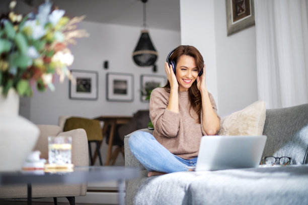 迷人的女人在家里放松，使用耳机和笔记本电脑图片下载
