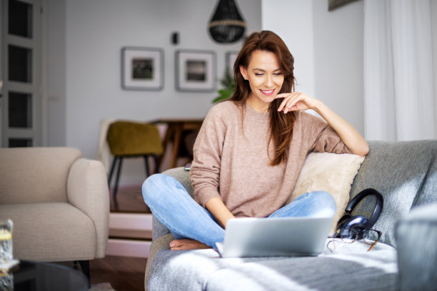 微笑的白人妇女使用笔记本电脑在家里坐在沙发上图片下载