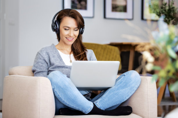 迷人的女人在家里放松，使用耳机和笔记本电脑图片下载