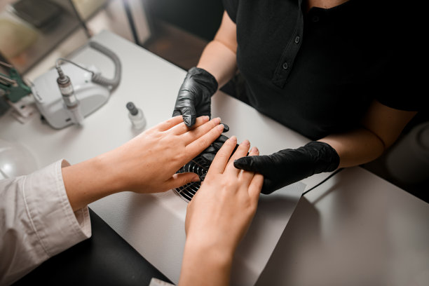 在美容院修指甲。戴着黑色手套的师傅握着客户的手。特写镜头。俯视图图片下载
