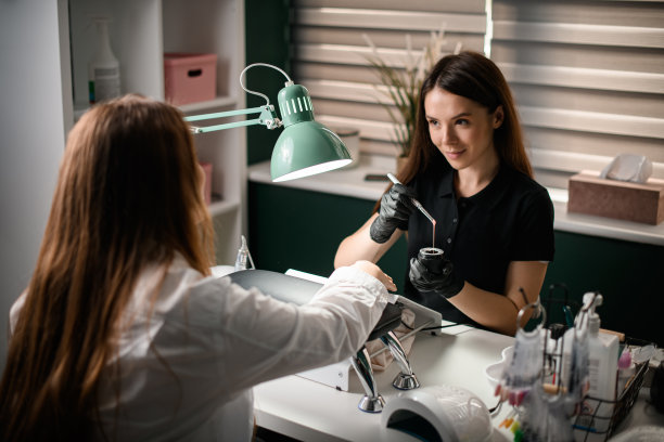 查看美甲师拿着罐子和刷子与啫喱指甲油和女客户在美容院图片下载