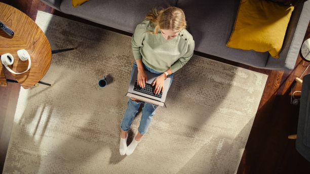 时尚的阁楼公寓内饰:年轻女子使用笔记本电脑坐在客厅的地毯上。创造性自由职业者在家远程工作。企业家做电子商务，网上购物。前视图。图片下载