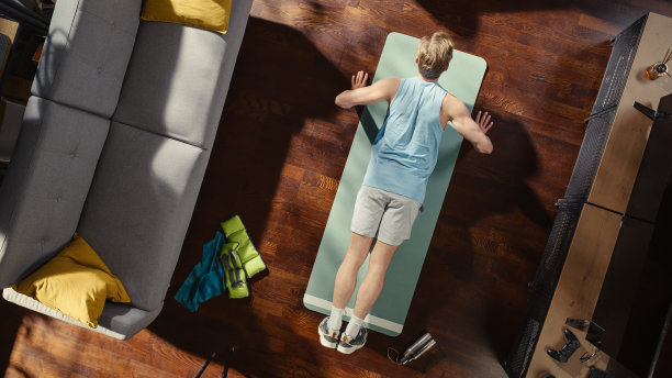 运动概念:有魅力的男人在家里的垫子上做俯卧撑运动。肌肉发达，非常强壮的运动员在他时尚的公寓客厅里锻炼。自上而下的上方拍摄。图片下载