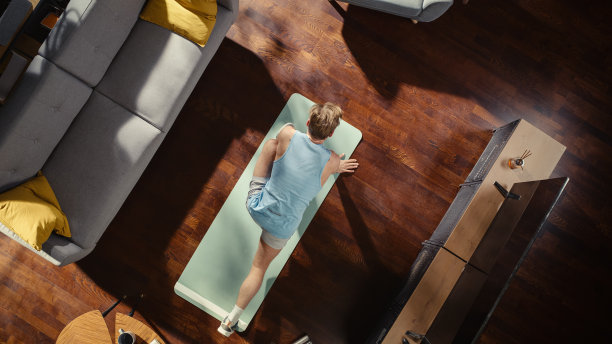 俯视图体育:有魅力的男人做瑜伽拉伸在家里的锻炼垫。肌肉发达、英俊的运动员在他时尚的公寓里健身。从上到下的起居室。图片下载