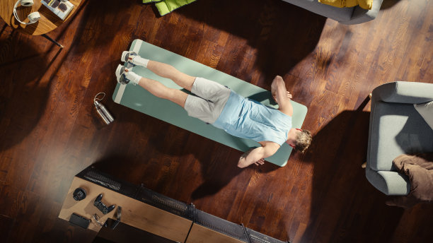 运动概念:有魅力的男人在家里的垫子上做俯卧撑运动。肌肉发达、健康、强壮的运动员在他时尚的公寓客厅里锻炼。自上而下的上方拍摄。图片下载