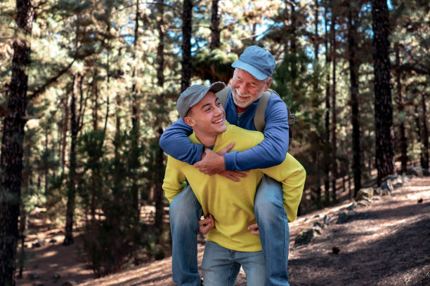 英俊的男孩背着爷爷在森林里快乐地走着。微笑的多代家庭夫妇一起享受山和自然。新一代帮助老一代图片下载