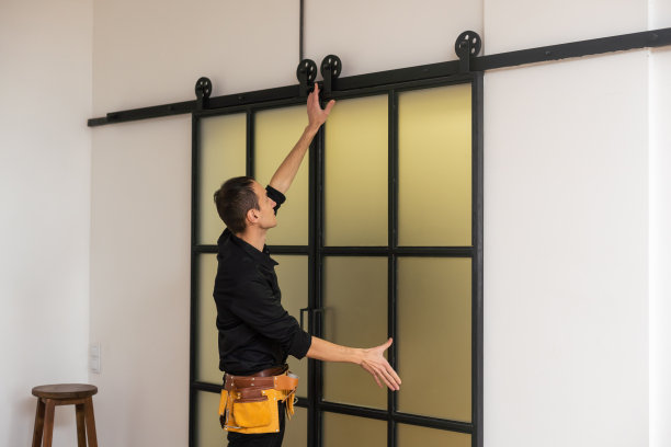 在新豪华公寓内，男工人正在安装带有木质框架的室内玻璃门。图片下载