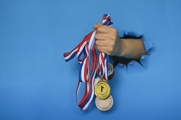 胜利或成功的概念。金牌，银牌和铜牌。在蓝色背景中，女性手从纸孔中拿着奖牌。图片下载