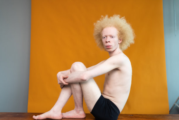 年轻人拥抱膝盖在橙色的背景图片下载