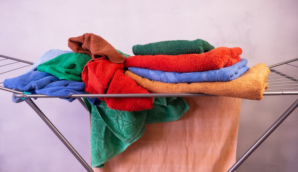干净的彩色毛巾挂在室内的烘干机上。现代烘干机的衣服在灰色的背景。洗衣后晾干衣服的装置。图片下载