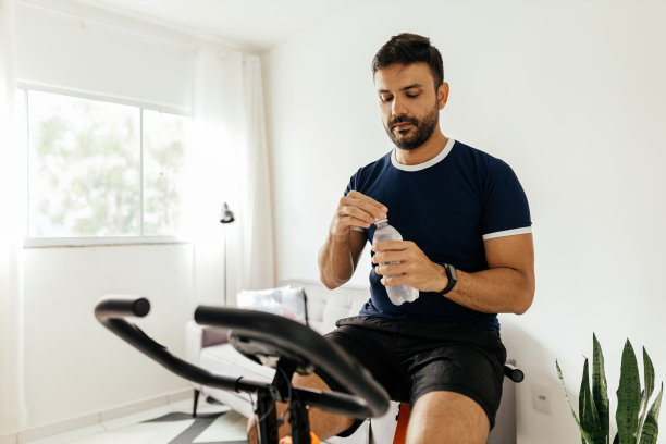 男子带着水瓶在家里的健身自行车上锻炼图片下载