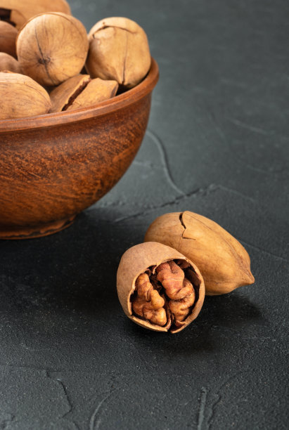 两个带壳的山核桃特写，一个碗放在深色混凝土背景上图片下载