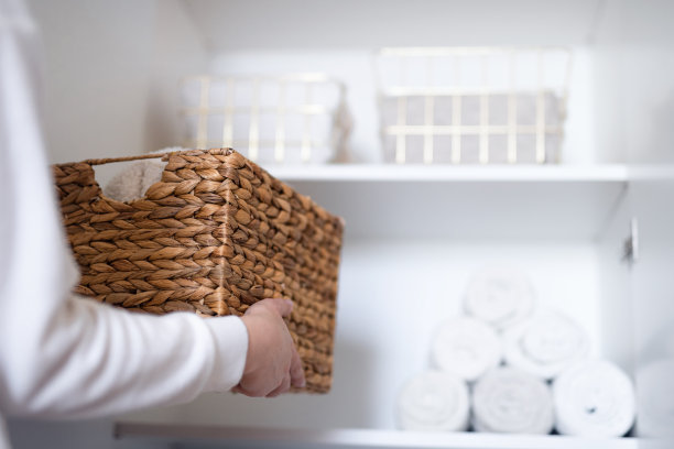 女人在打开的白色衣柜的架子上整理衣服，把洗好的衣服叠在篮子里。空间组织与存储系统。图片下载