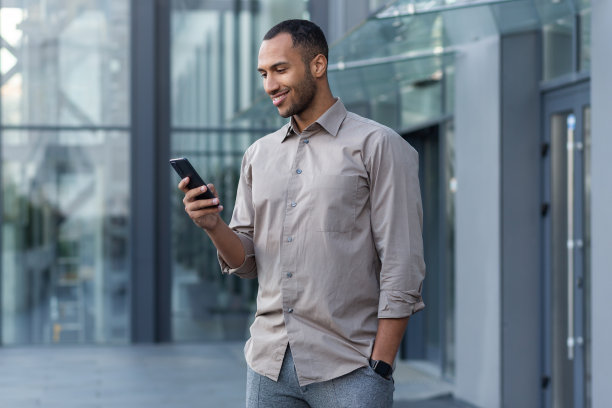 一名年轻的西班牙裔男子站在街上，手里拿着电话，正在使用并微笑图片下载