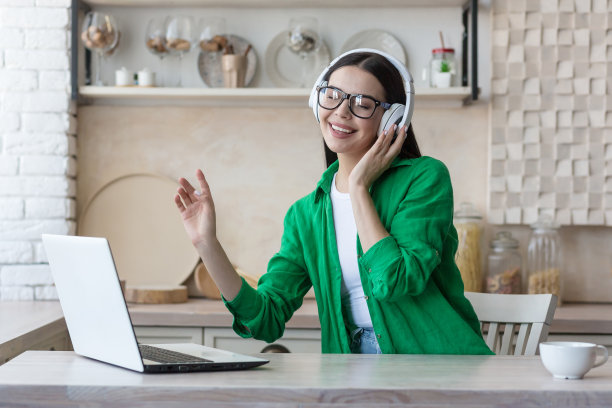 一名年轻女子戴着白色耳机听音乐。她坐在家里用笔记本电脑图片下载