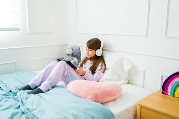 可爱的年轻女孩穿着睡衣在床上看电影图片下载