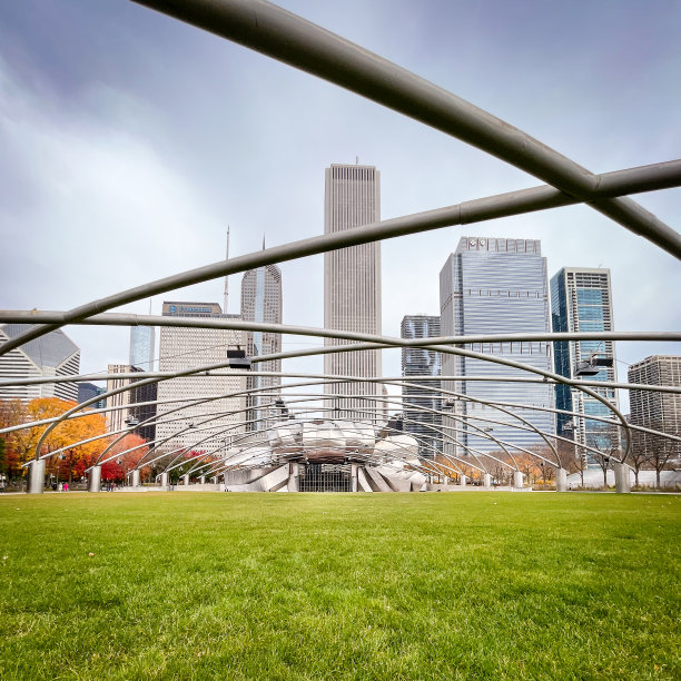 在一个深秋的日子里，芝加哥千禧公园里的杰伊·普利兹克馆，从远处向北看，天空充满威胁。背景是摩天大楼，前景是金属横梁，穿过空旷的绿色草坪，穿过照片走向展馆。图片下载