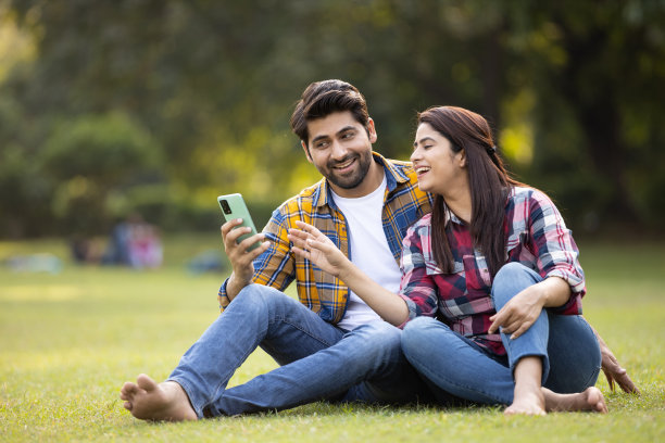年轻夫妇在公园玩智能手机。库存图片图片下载