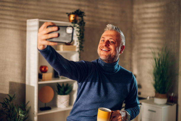 中年男子一边在家喝咖啡一边用智能手机自拍图片下载
