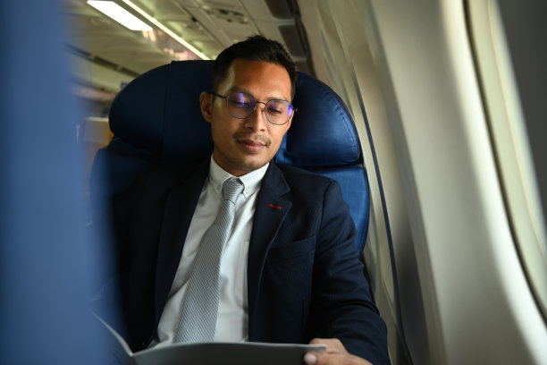 身着正装的亚洲商人坐在飞机的窗户边阅读财务文件。图片下载