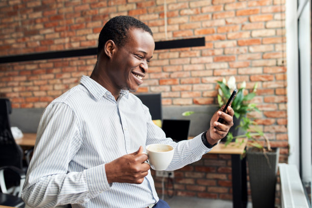 在小办公室里喝咖啡休息时间打电话的笑商人图片下载