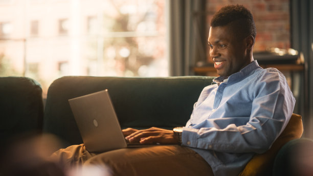 集中的黑人男性在家工作，使用笔记本电脑。在键盘上打字和浏览网页。自由职业者和千禧一代专业人士的概念。图片下载