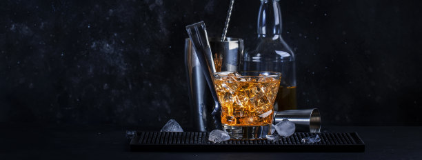 用苏格兰威士忌、苦杏仁酒和冰块调制的教父酒精鸡尾酒。黑色吧台背景，钢条工具，复制空间横幅图片下载