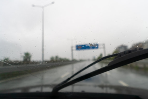 雨天被飞石砸破的汽车挡风玻璃。玻璃上有洞，碎片和碎片，玻璃条上有裂缝。一辆挡风玻璃被石头砸坏的汽车图片下载