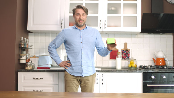 一个年轻人在厨房里拿着一个绿色的东西，展示一个产品，微笑着展示一个令人愉快的、想象中的物体。图片下载