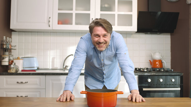 一个年轻人把锅放在厨房炉子上的餐桌上。图片下载