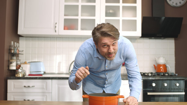 一个年轻人把锅放在厨房炉子上的餐桌上。图片下载