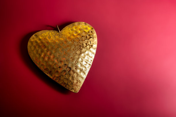 金色心形由金属制成，红色背景，情人节或母亲节贺卡，爱的象征，复制空间图片下载