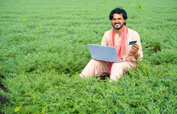 年轻农民在田间使用笔记本电脑上的信用卡进行在线支付——现代农业、网上银行服务和无线技术的概念图片下载