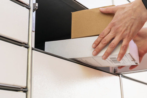 拿着纸板箱的人。在自助邮件终端机旁，一个女人手里拿着一个盒子。包裹投递机。邮件递送和邮政服务，网上购物，电子商务概念图片下载