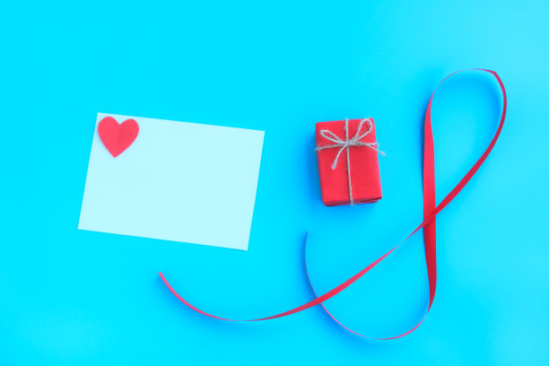 红色礼盒，红色丝带和白色贺卡与红色心形剪纸在蓝色背景，情人节快乐，爱和情人节概念。图片下载