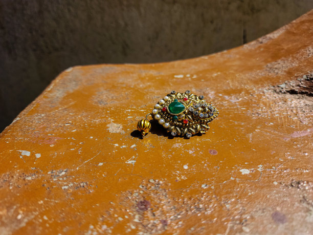 库存照片美丽的金色纱丽针或胸针装饰珍珠，红色，白色的石头，绿色的石头中间的针。在明亮的阳光下拍摄的照片。纱丽滴针图片下载