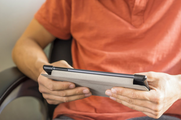 年轻人坐在扶手椅上使用平板电脑，双手在数字平板设备上输入文字信息图片下载