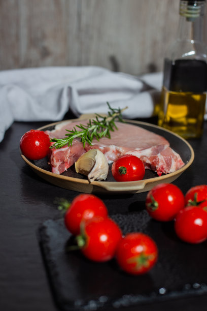 垂直拍摄的猪肉牛排，樱桃番茄，迷迭香，和大蒜在煎锅里图片下载