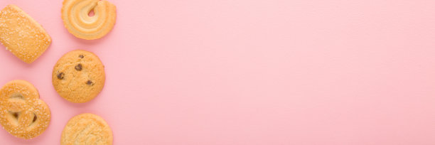 不同的干黄油饼干在浅粉色的桌子背景。柔和的颜色。特写镜头。甜的零食。宽横幅。文本的空白位置。自顶向下视图。图片下载