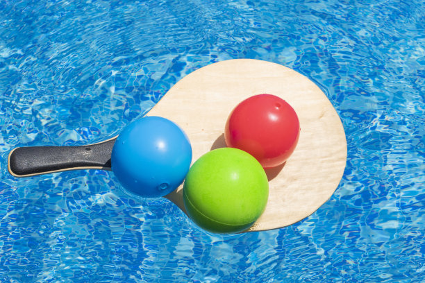 夏日游玩和度假乐趣，水上游戏，沙滩活动和运动概念。沙滩网球拍上的彩色球漂浮在游泳池的蓝色水中。图片下载