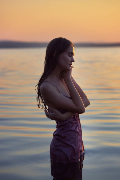 美丽的年轻女子在湖水中夏装日落。一个浪漫的湿女孩的肖像在日落，温暖的太阳，自然的美丽的女人图片下载