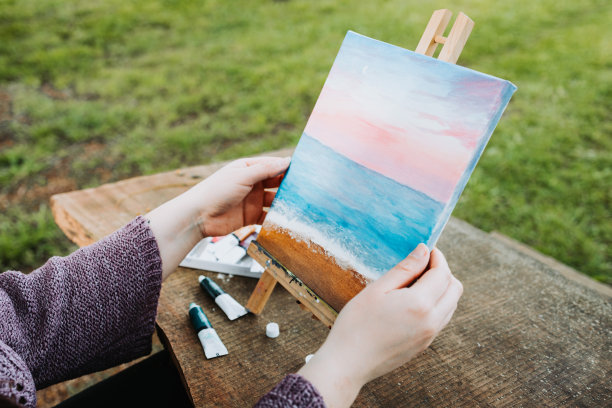 一位面目全非的年轻女艺术家在户外画布上用油画描绘自己的海滩风景。业余的画家。图片下载